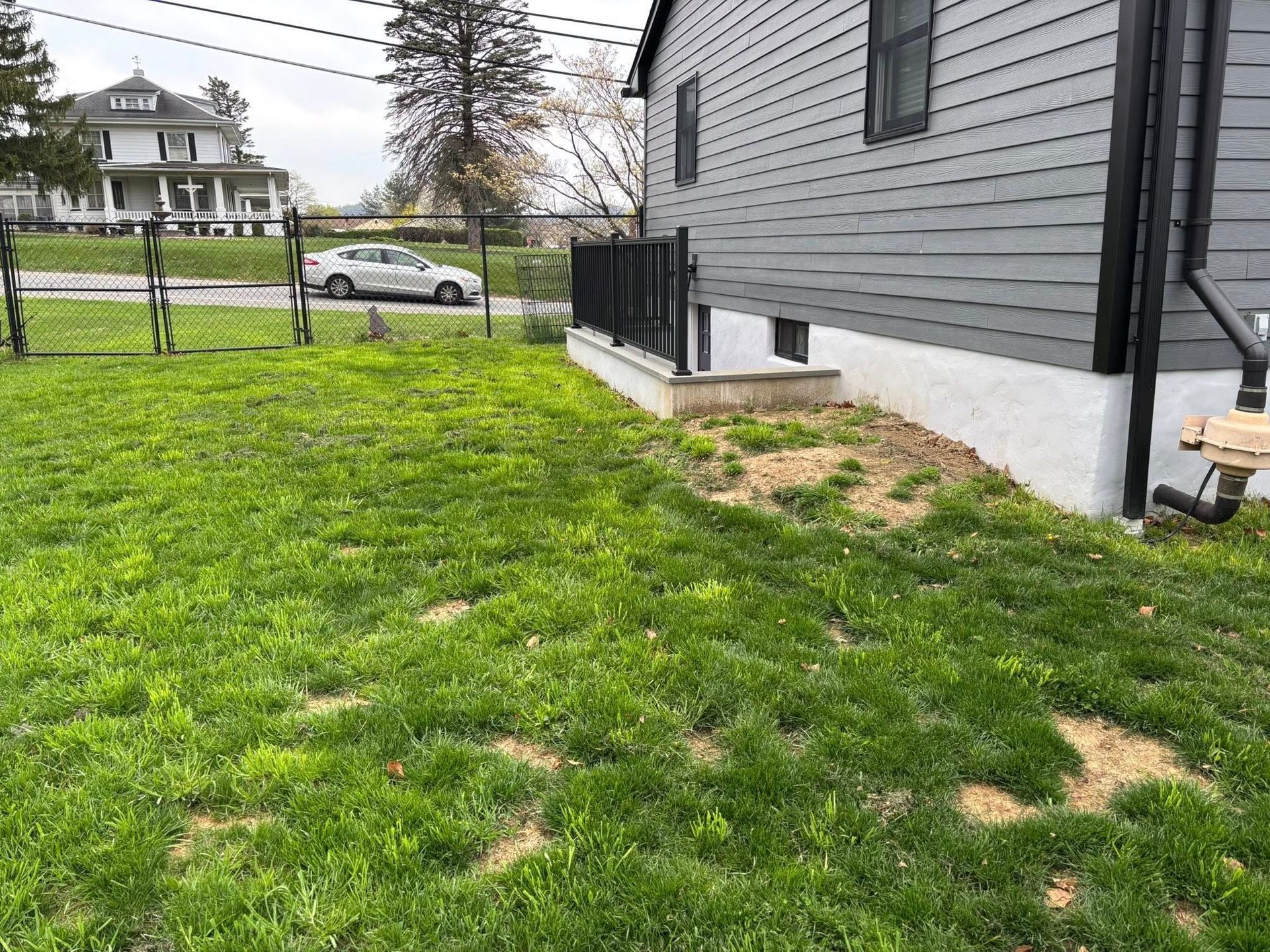A grey house with black trim and a grassy lawn. A low retaining wall is visible.