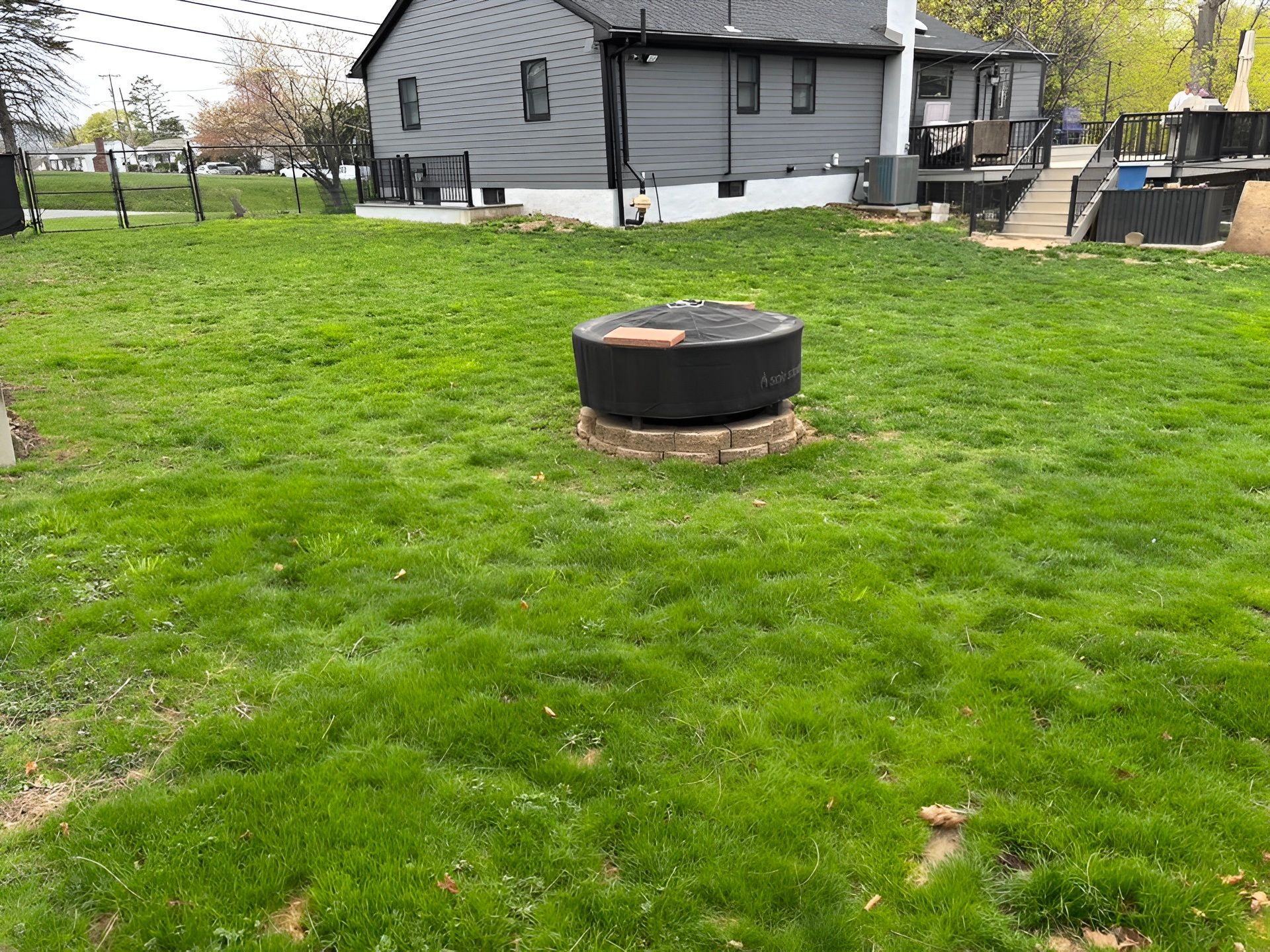 Backyard with fire pit, green grass, and gray house.