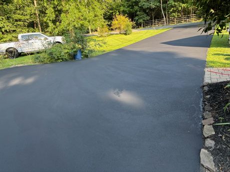 Newly paved black asphalt driveway bordered by grass and landscaping.