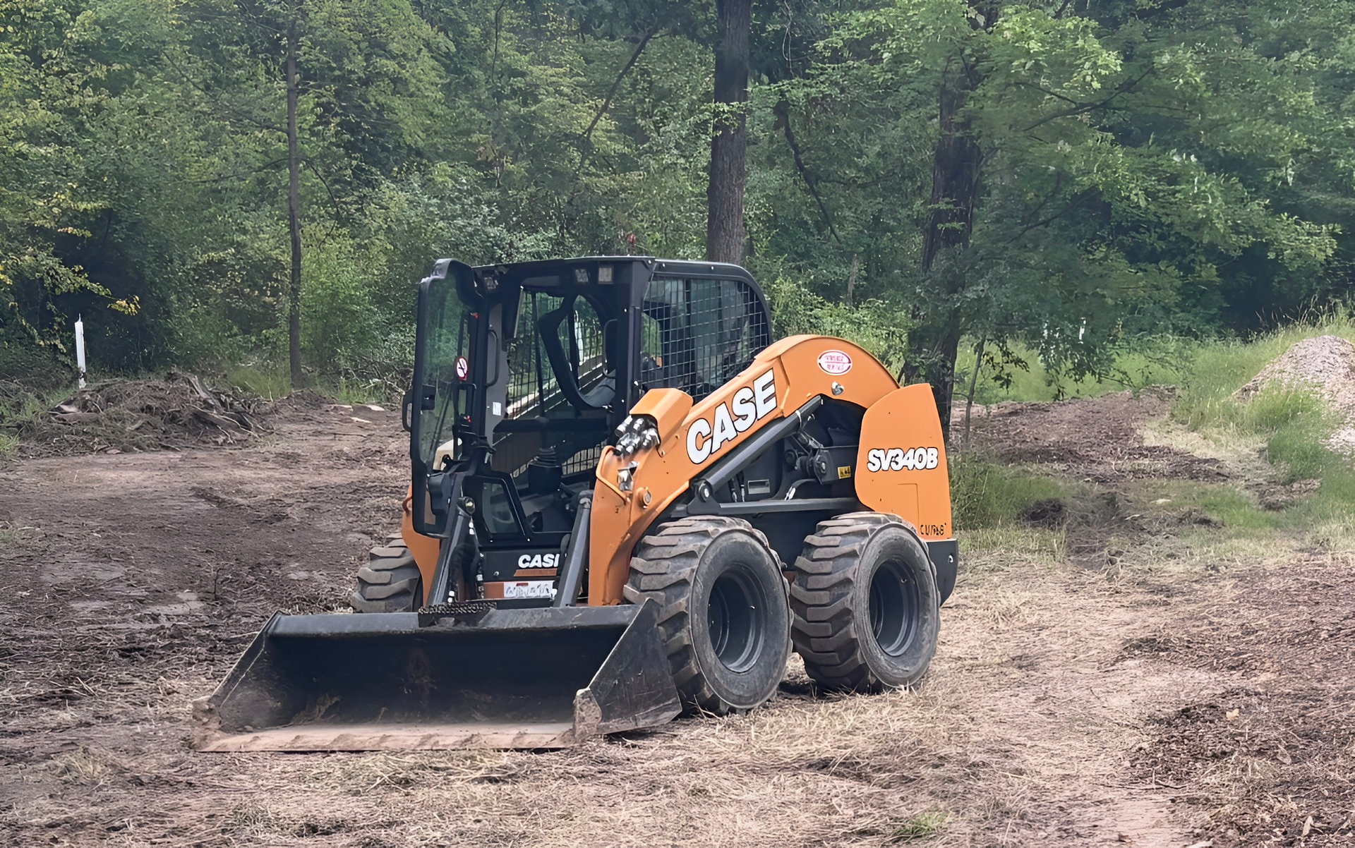 Orange Case skid steer loader in a clearing, with trees in the background.
