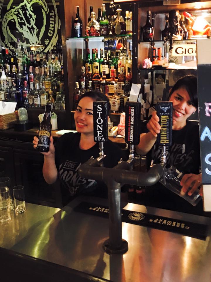 Two women behind a bar holding bottles of madness beer