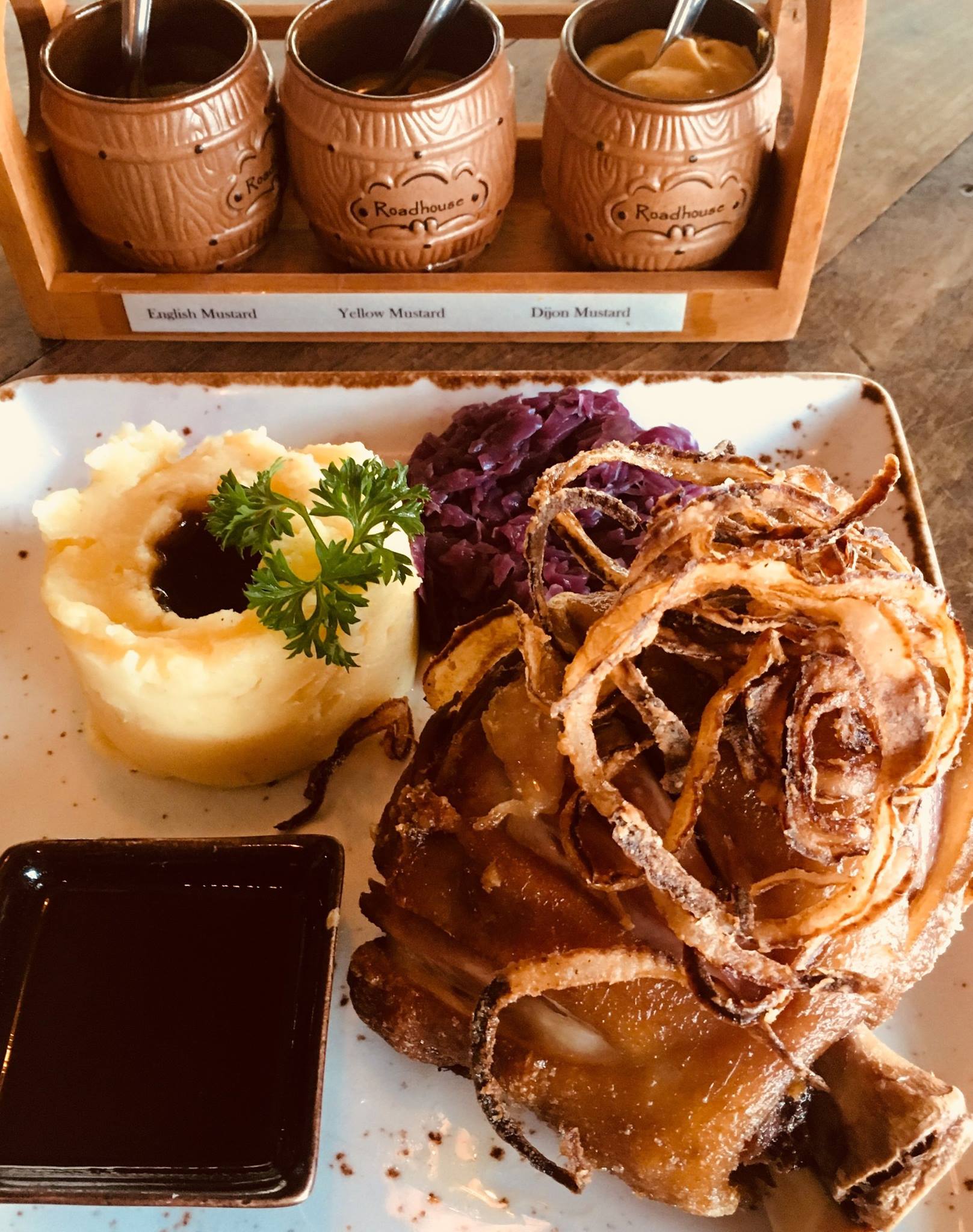 Pork Knuckle with mashed potatoes , onions , and sauce on a table.