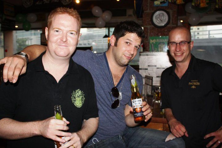 Three men are posing for a picture and one is holding a bottle of corona beer