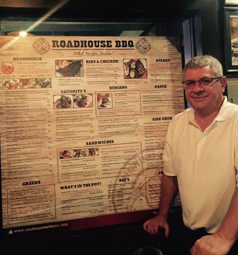 Owner/Chef in front of a big menu for roadhouse BBQ