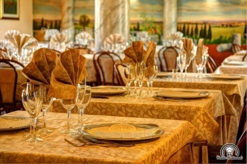 Dei tavoli apparecchiati con delle tovaglie di color beige, dei piatti e bicchieri