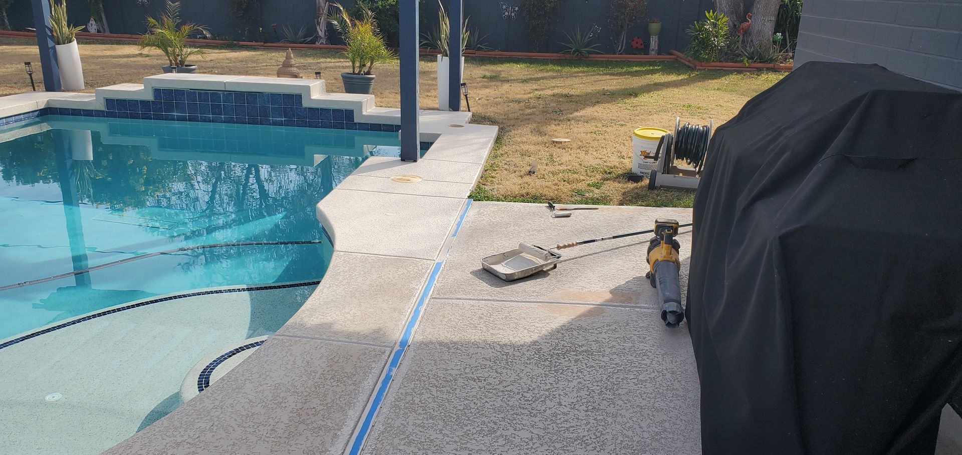 A patio with a grill and a swimming pool in the background.