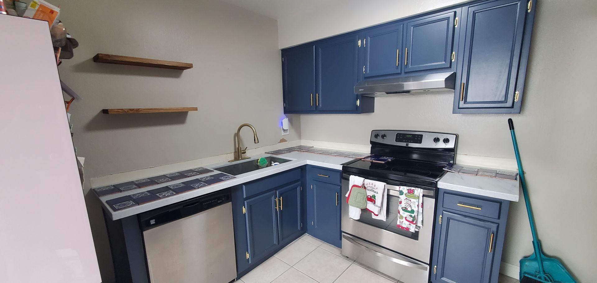 A kitchen with blue cabinets , a stove , a sink and a mop.
