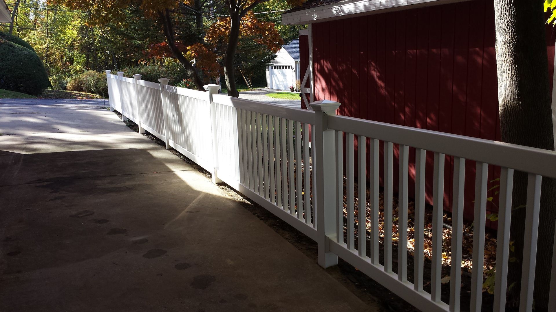 A white fence along a driveway next to a red barn.