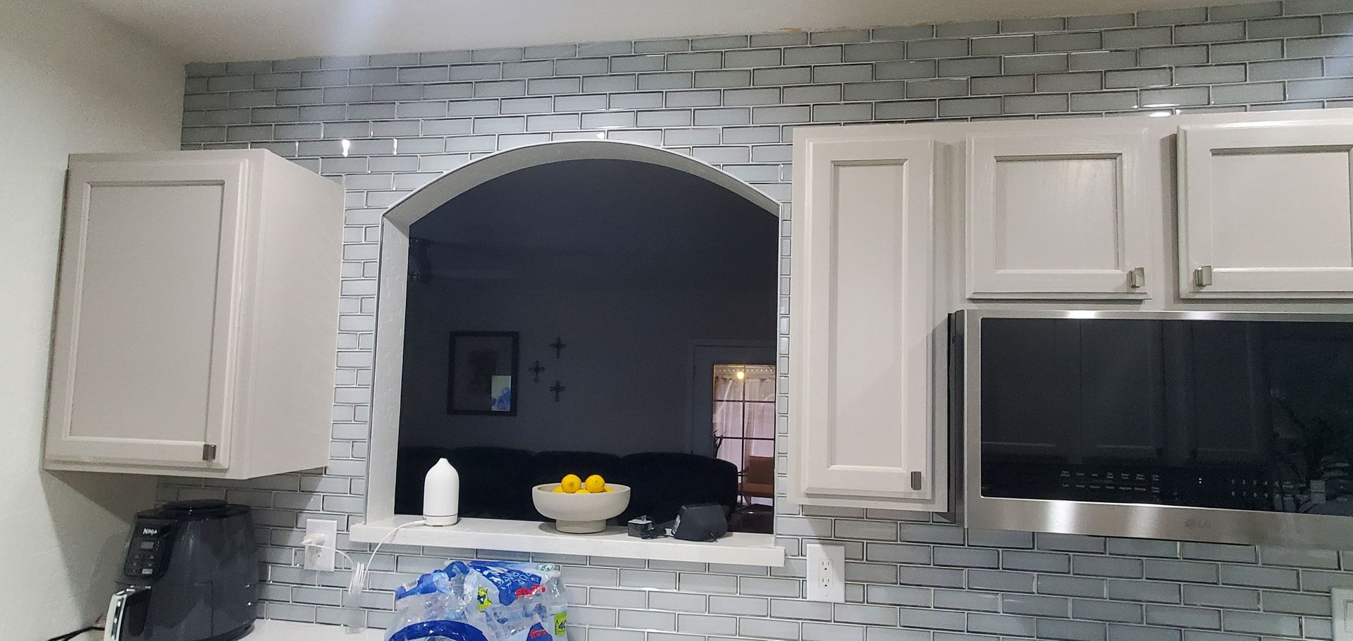 A kitchen with white cabinets , stainless steel appliances , a microwave and a window.