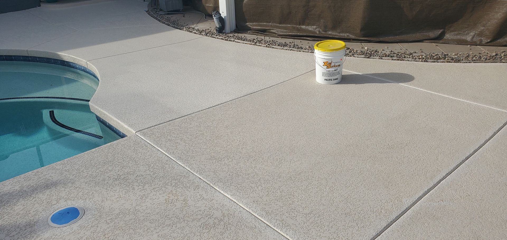 A bucket of bleach is sitting on the ground next to a swimming pool.
