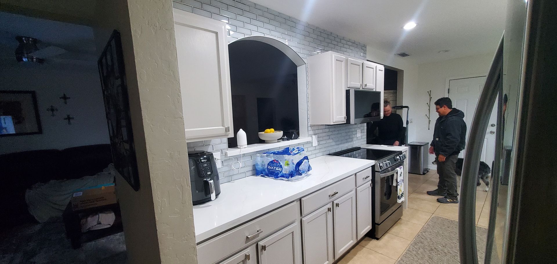 A man is standing in a kitchen next to a refrigerator.