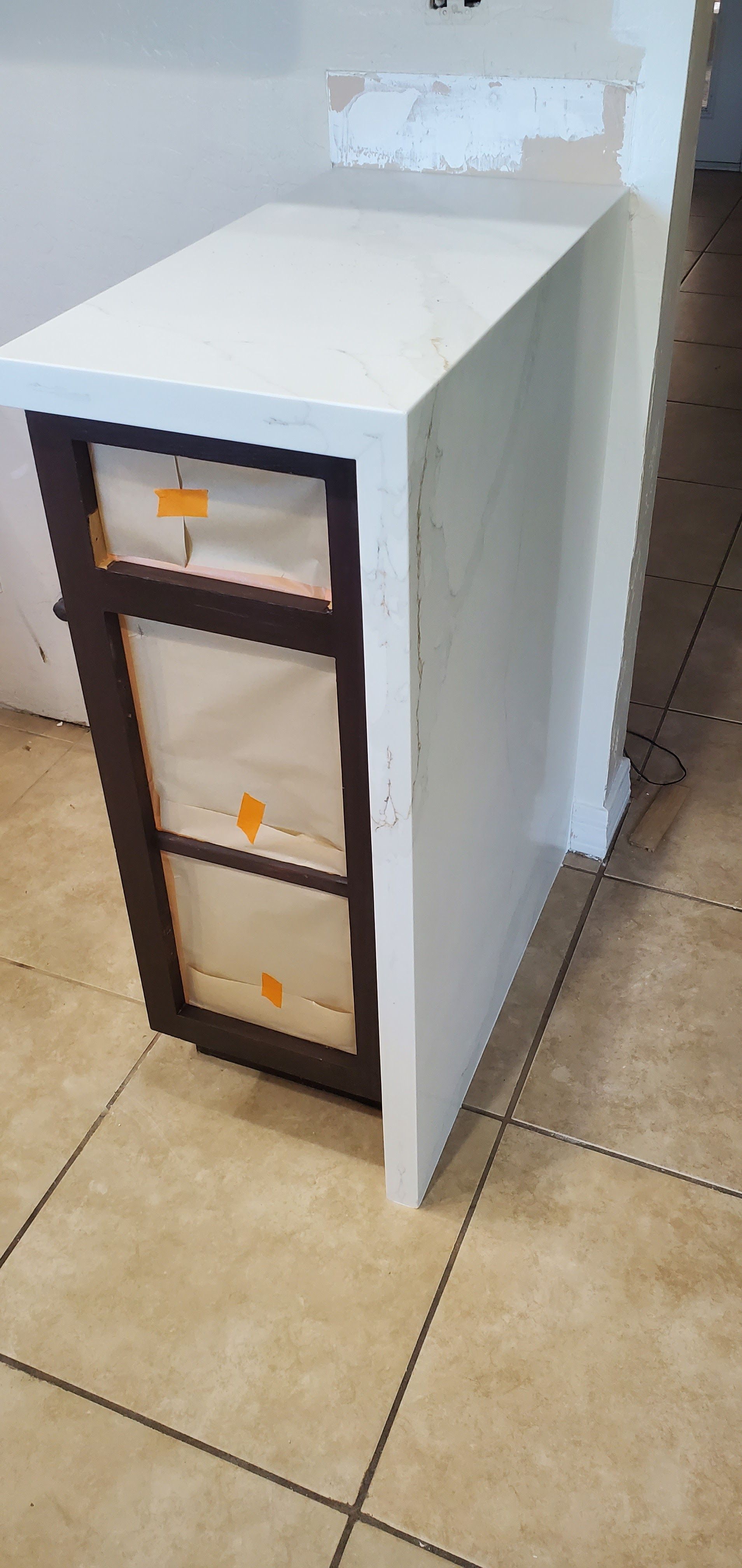 A white cabinet with three drawers is sitting on a tiled floor.