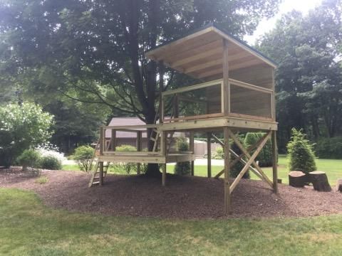 A wooden tree house is sitting under a tree in a yard.