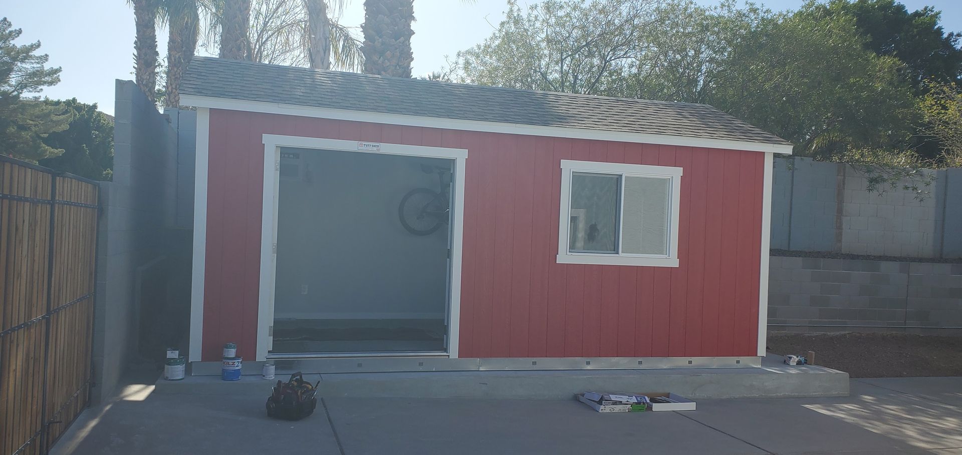 A red shed with a white trim is being painted in a backyard.