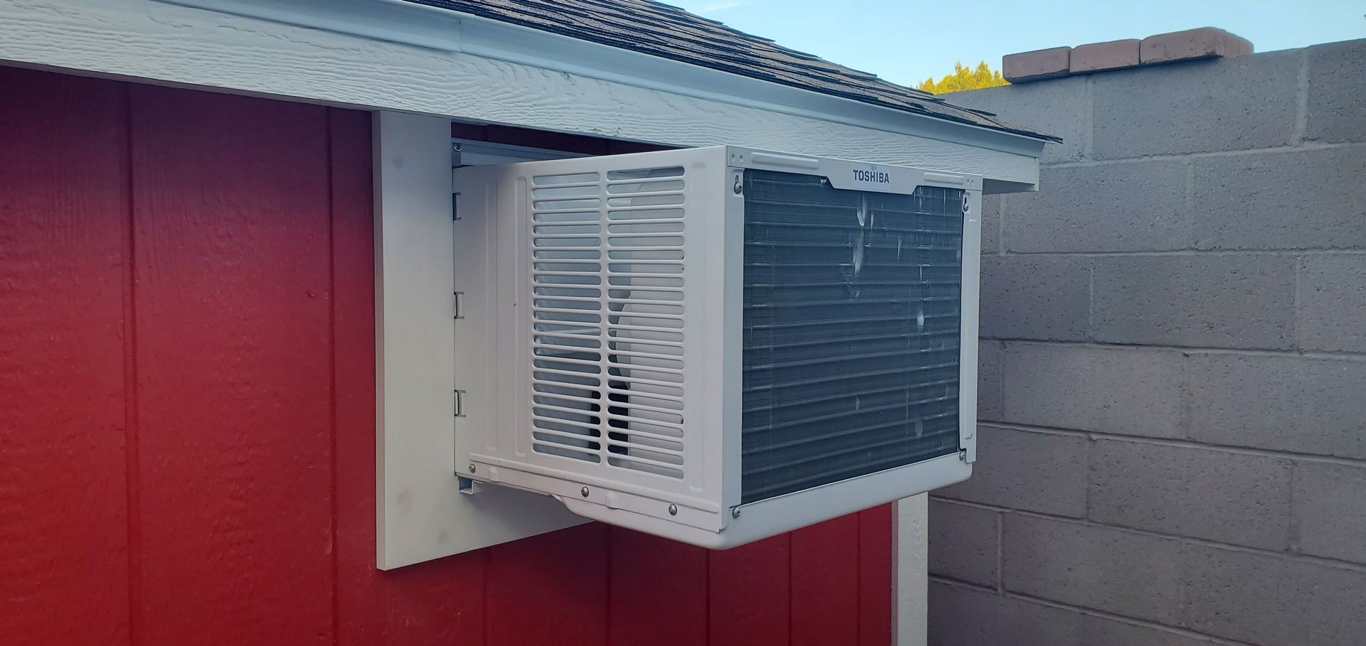 A small air conditioner is mounted on the side of a red building.