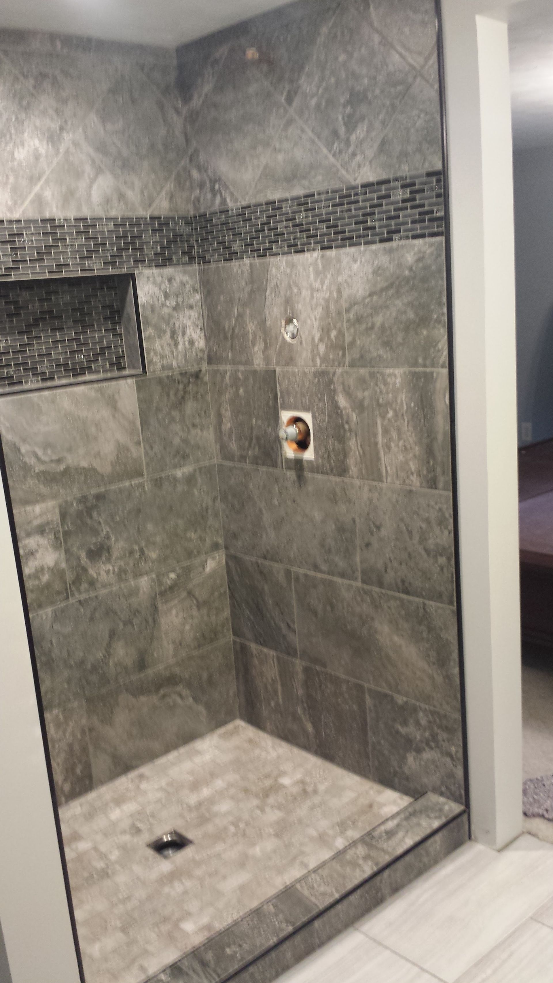 A bathroom with a walk in shower and a gray tiled wall.