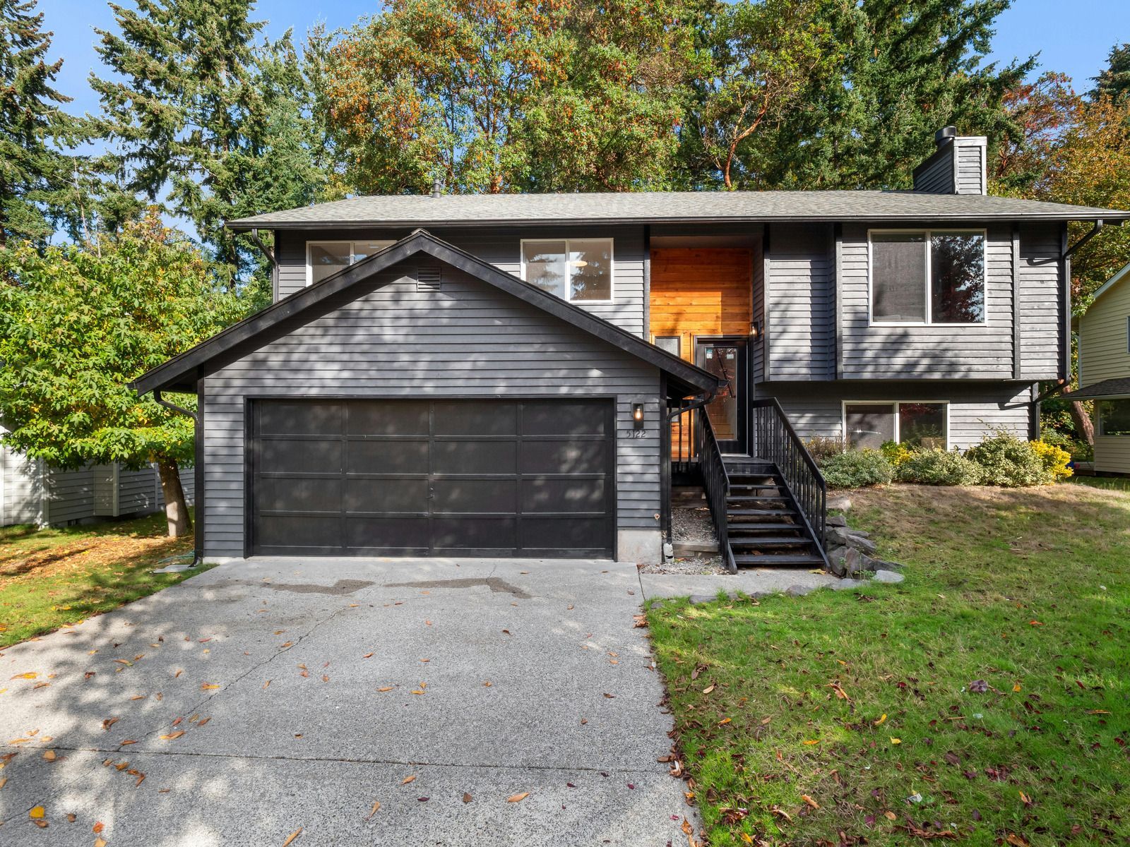 A gray house with a black garage door and stairs