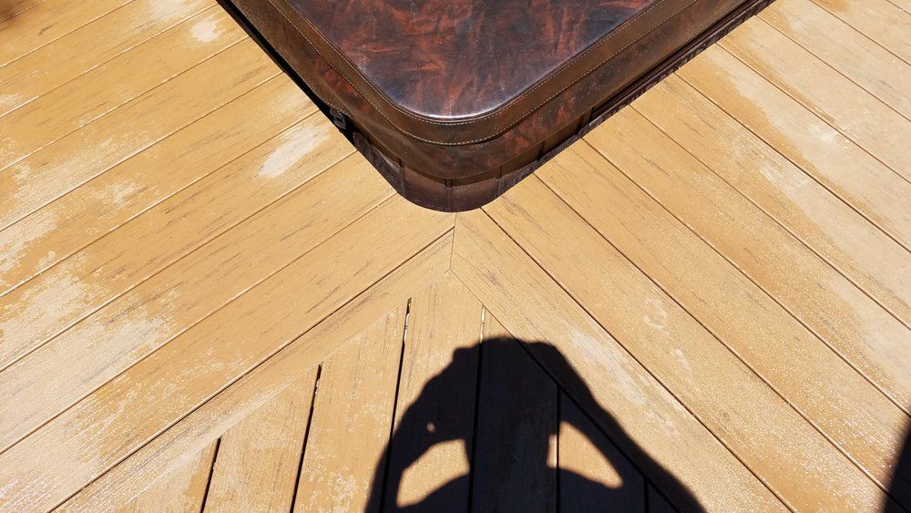 A shadow of a person is cast on a wooden deck next to a hot tub.