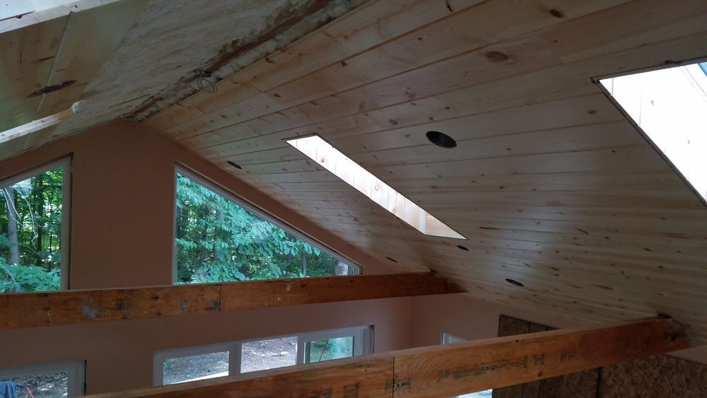 A wooden ceiling with a skylight in a room with a lot of windows.
