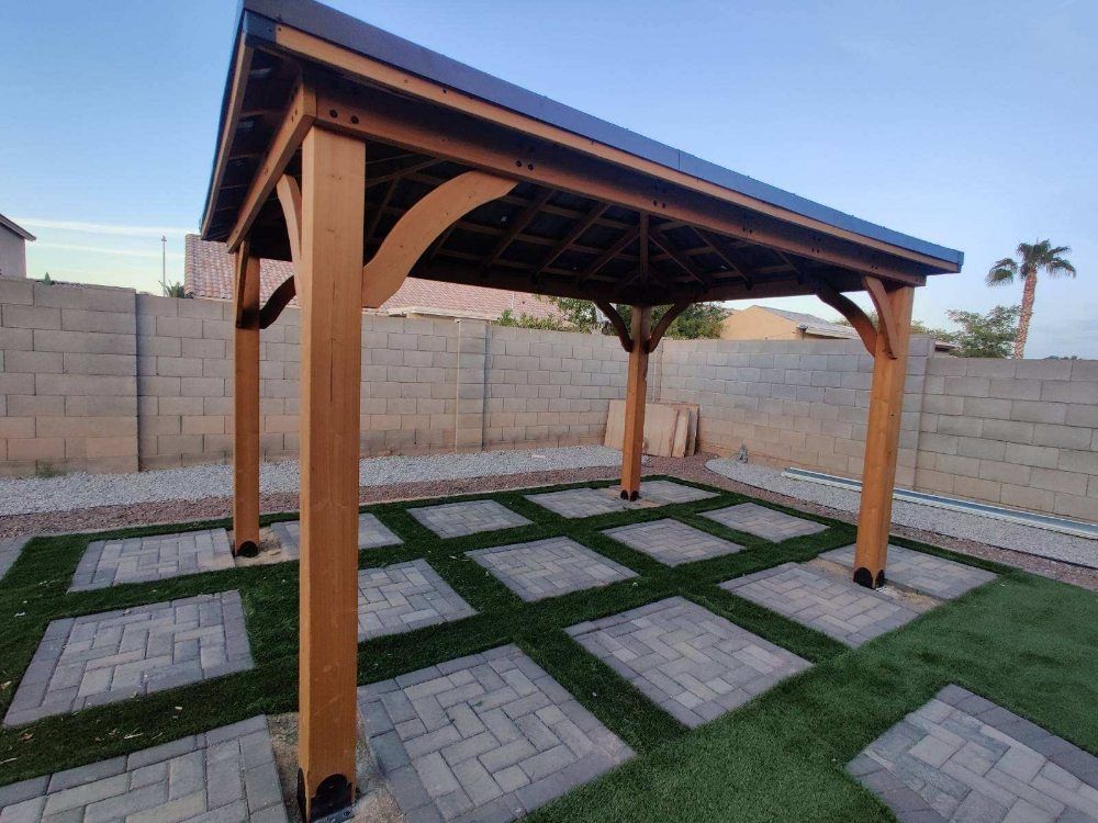 A wooden gazebo is sitting on top of a brick patio in a backyard.
