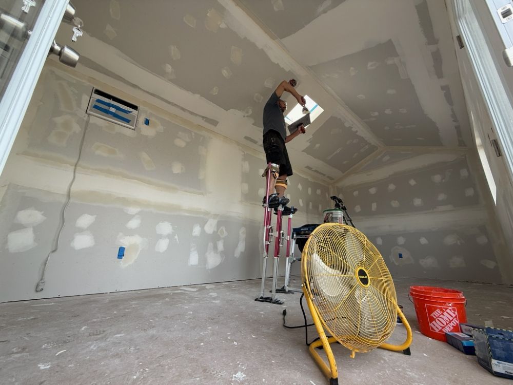 A man is standing on a ladder in a room with a fan.