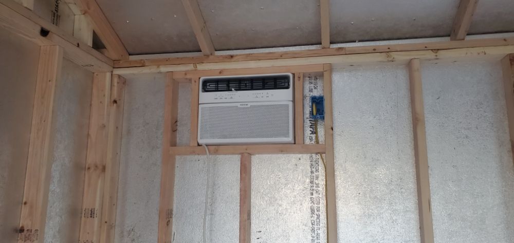 A small air conditioner is mounted on the wall of a room under construction.
