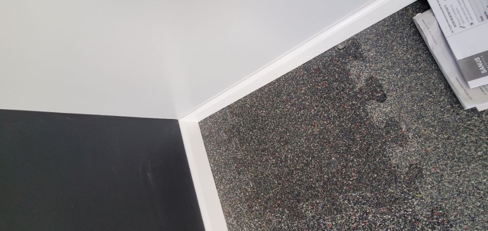 A corner of a room with a gray carpet and a white trim.