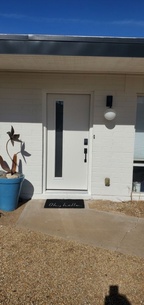A white house with a black door and a blue potted plant in front of it.