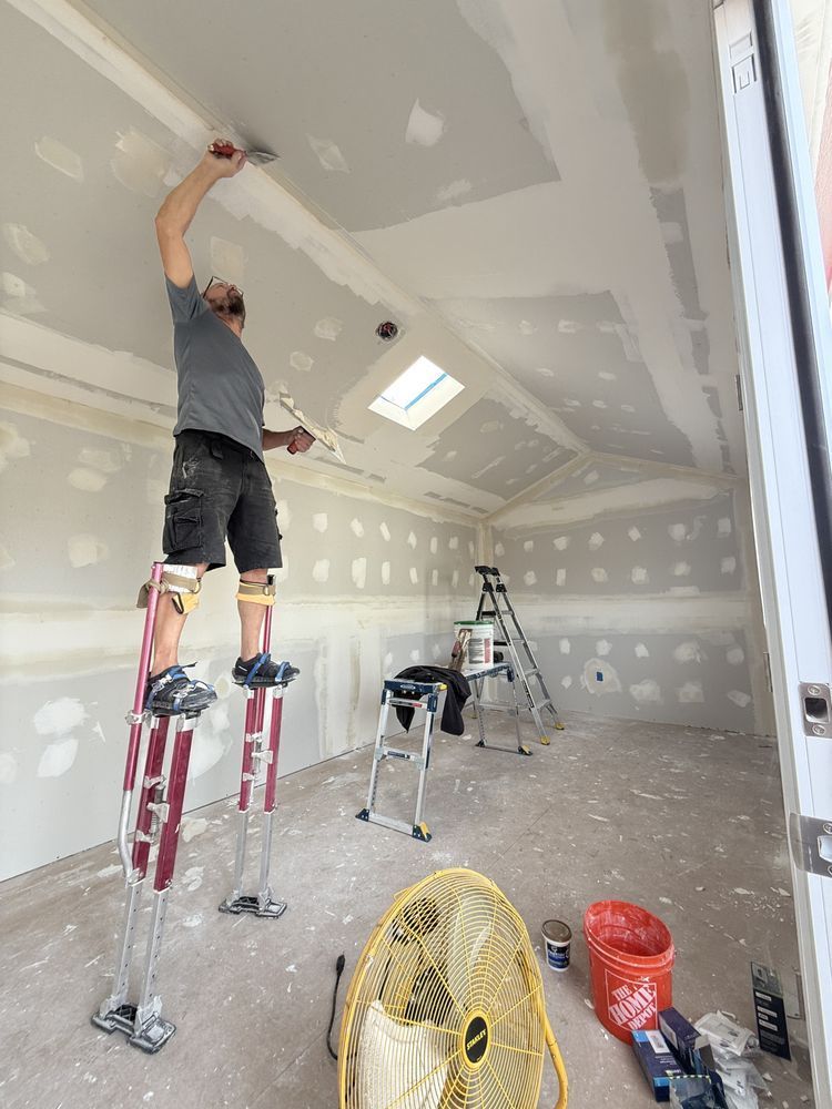 A man is standing on a ladder painting the ceiling of a room.