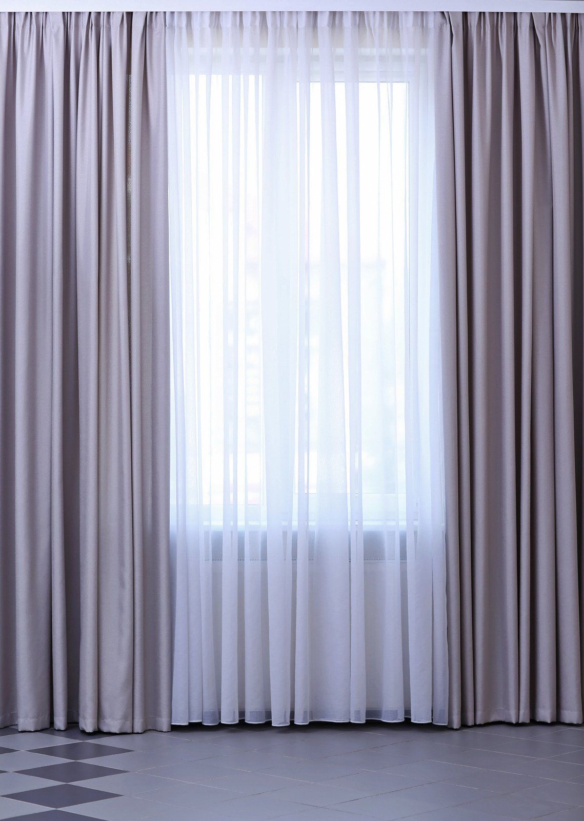 A window framed by gray curtains and sheer white curtains. The room has a gray and patterned floor.