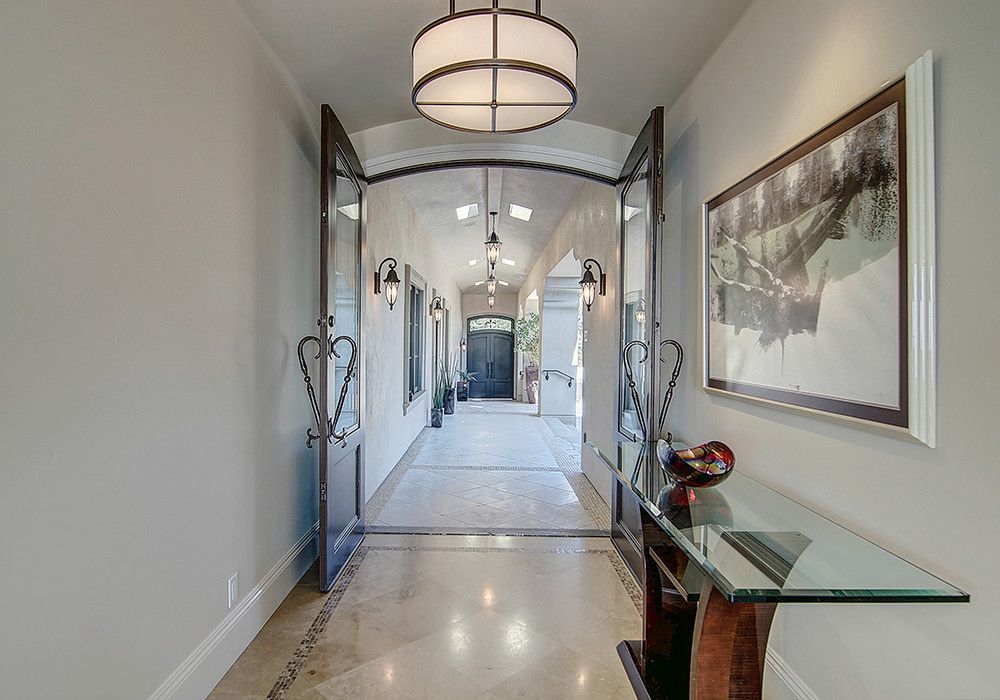 Hallway with open iron doors, decorative lighting, artwork, and a glass-top table. Light-colored walls and floor.