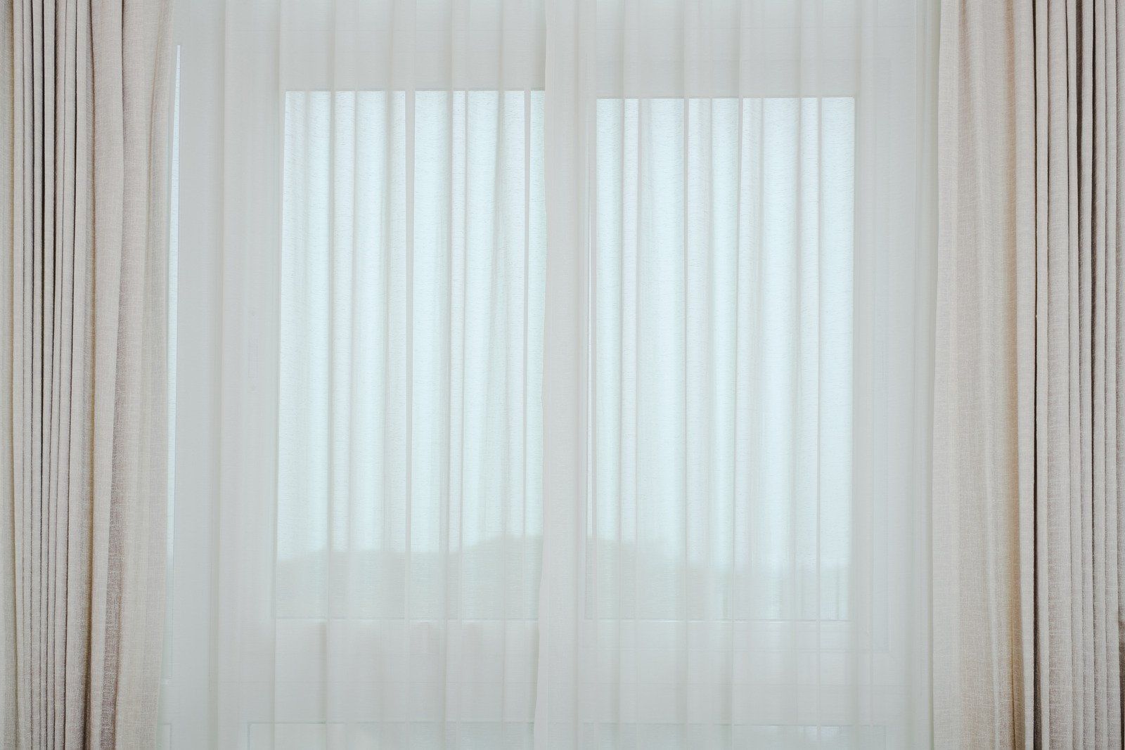 Light streams through a window covered by sheer white curtains and beige drapes.