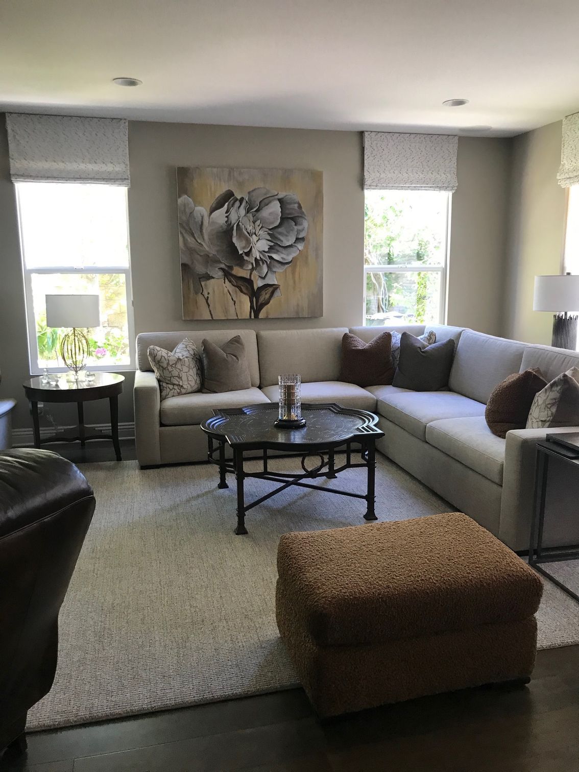 Living room with a beige sectional sofa, floral artwork, and a round coffee table on a beige rug.