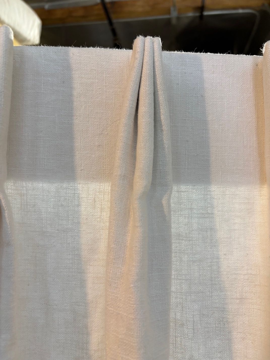 Close-up of a white, textured curtain, with a vertical pleat, hanging in front of a window.