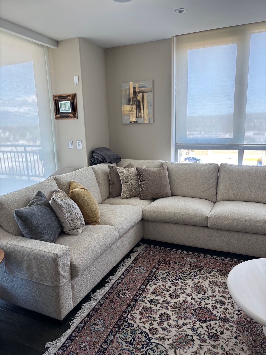 A beige sectional sofa with decorative pillows sits on a patterned rug in a w