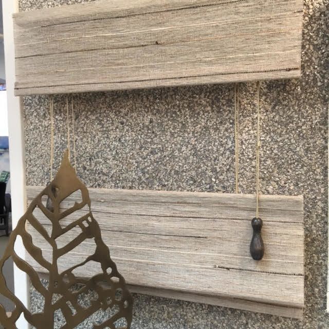 Close-up of two layered, rustic-looking window blinds made of textured fabric. A decorative metal leaf is in the foreground.