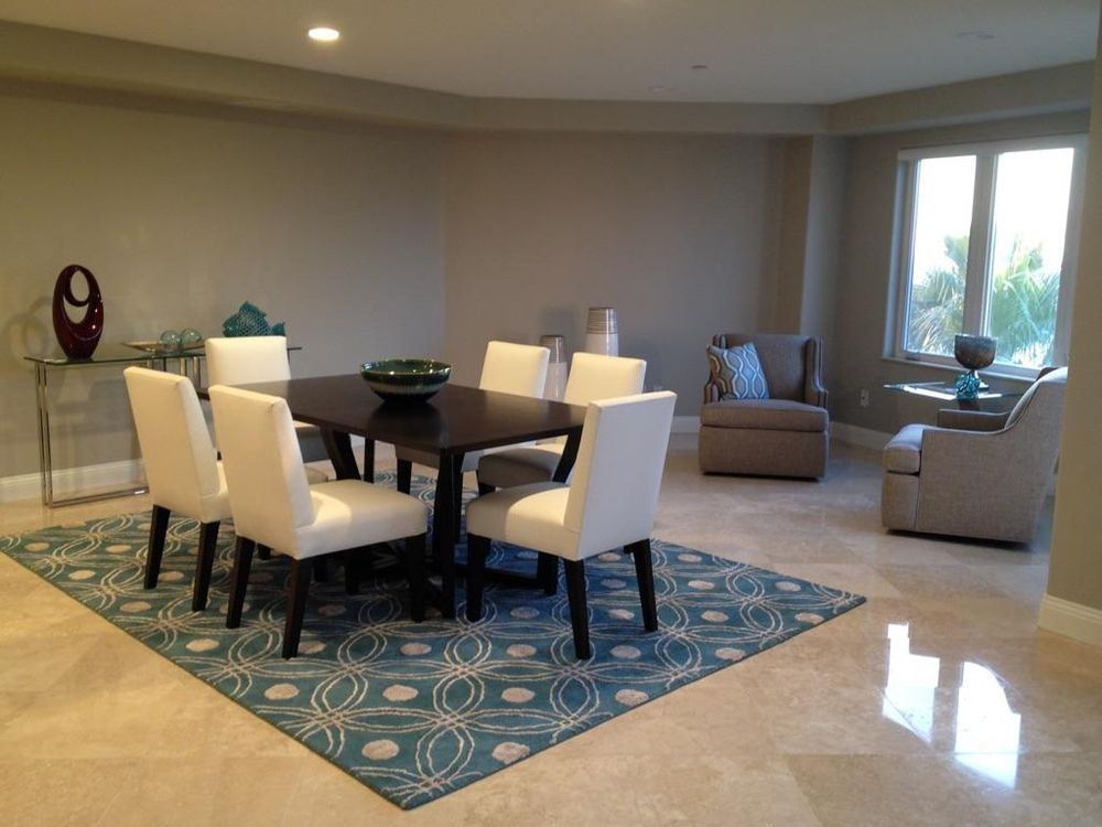 A modern dining room with a dark wood table and white chairs on a blue patterned rug, with seating area.