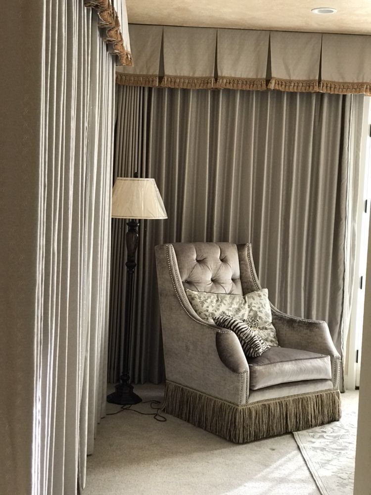 A luxurious interior features a tufted armchair with fringe, a floor lamp, and flowing gray curtains.