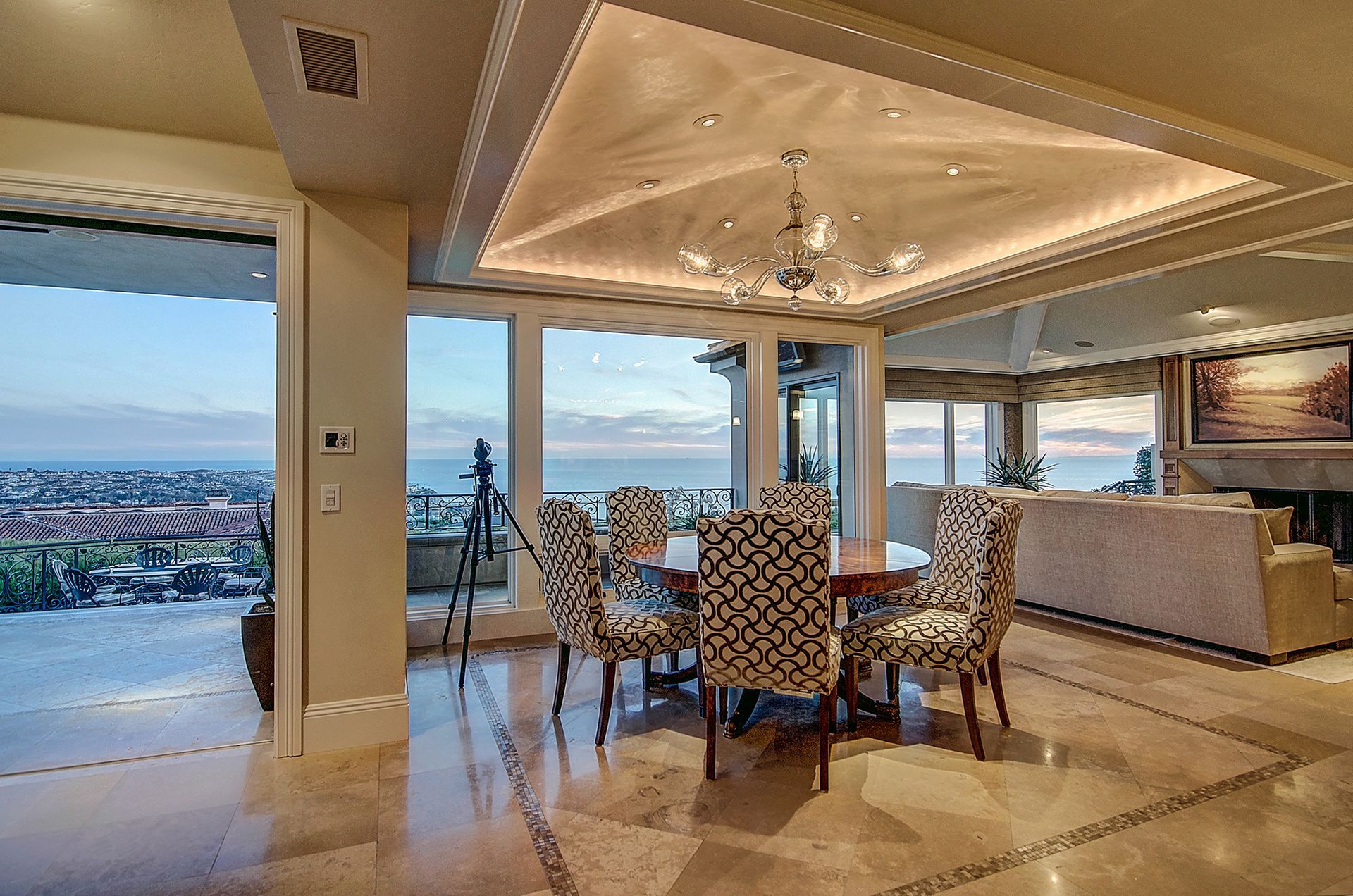 Elegant dining room with a round table set for six, overlooking a coastal view. Features patterned chairs