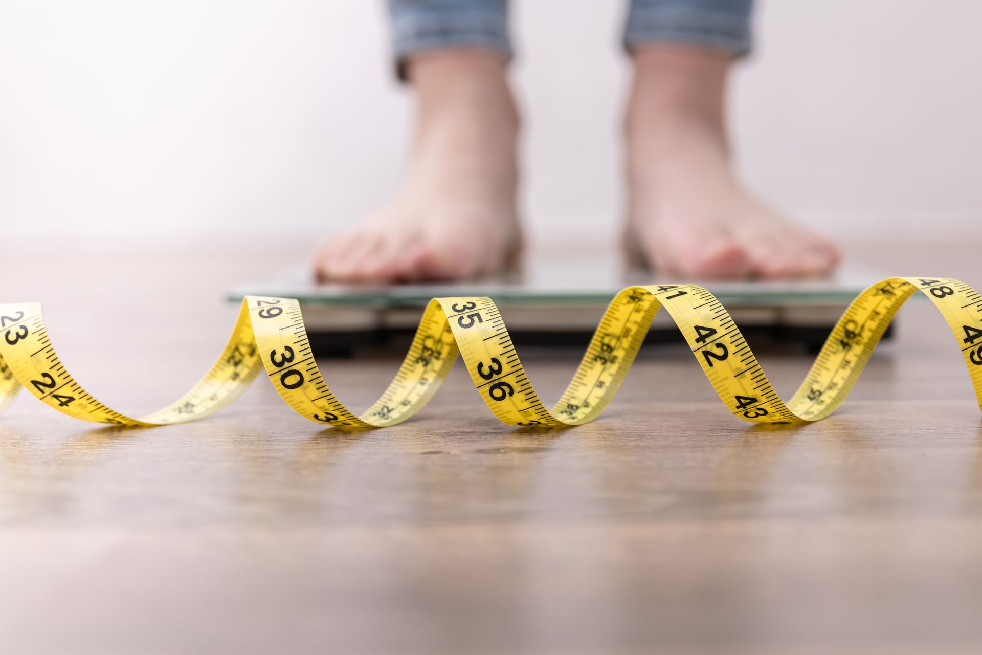 A person is standing on a scale next to a measuring tape.