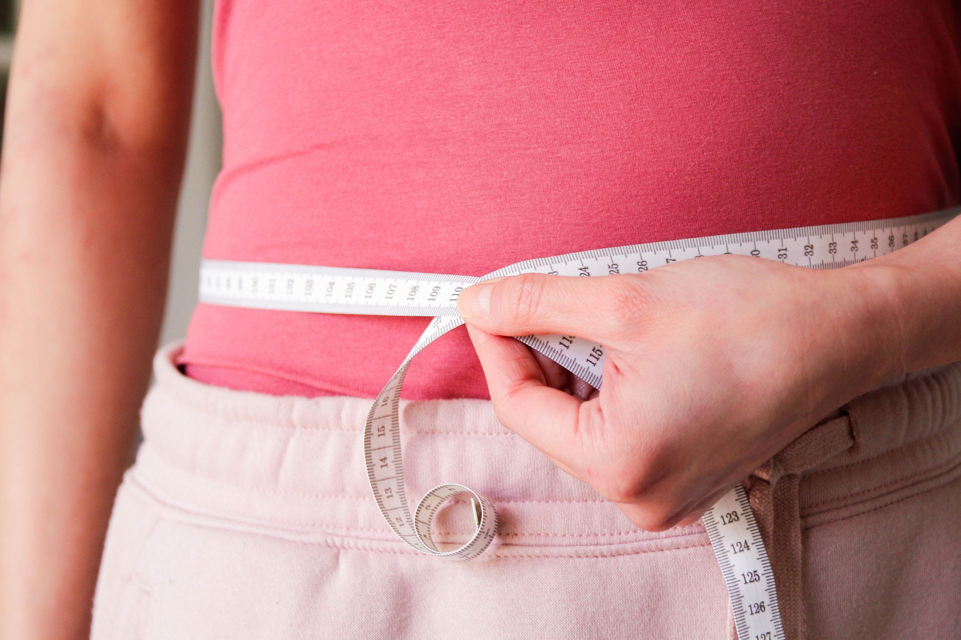 A woman is measuring her waist with a tape measure.