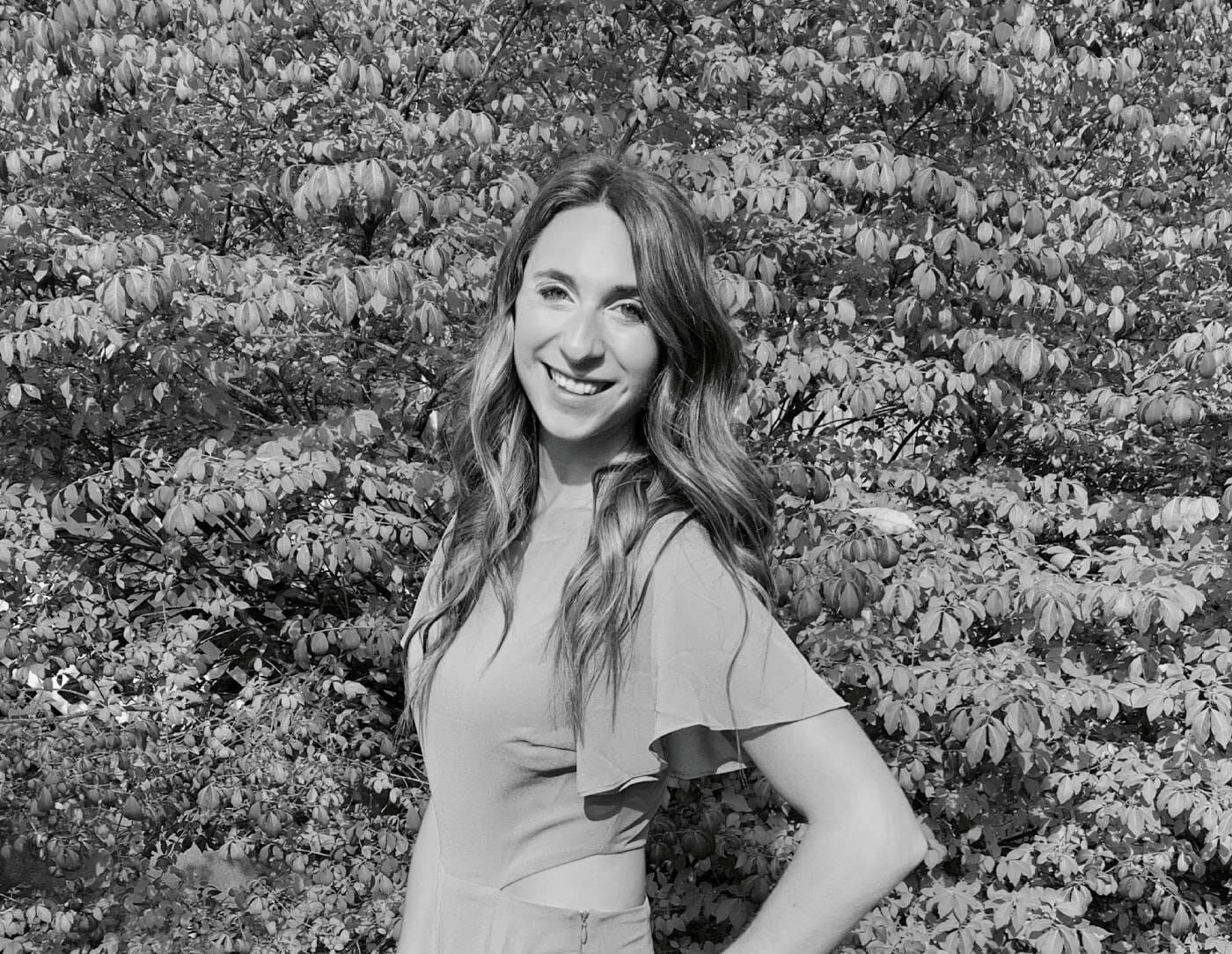 A black and white photo of a woman standing in front of a bush.