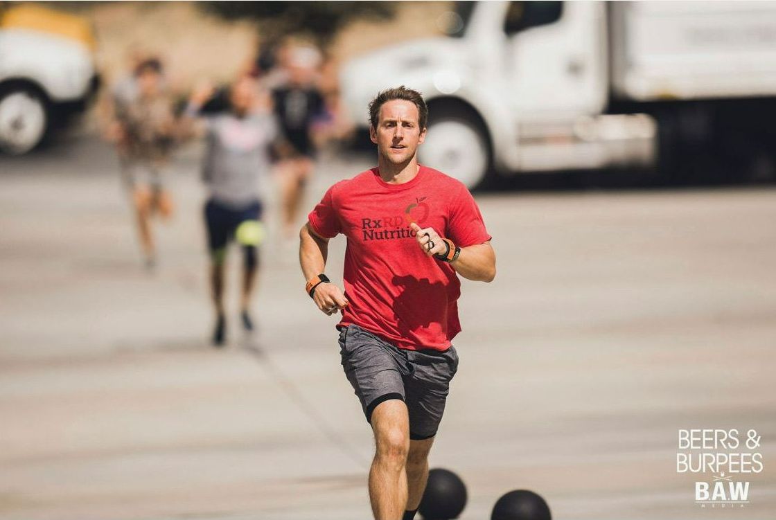 A man in a red shirt is running with a truck in the background.
