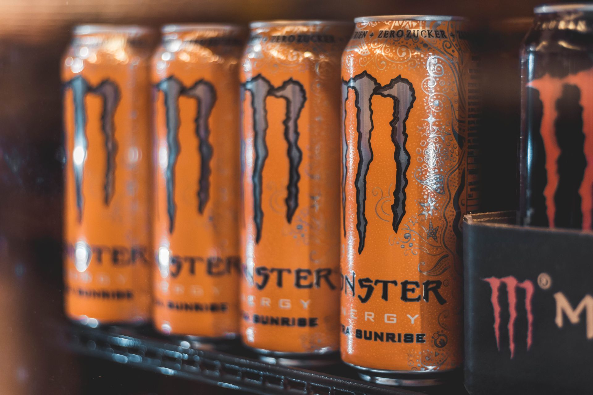 A row of monster energy drinks are lined up on a shelf.