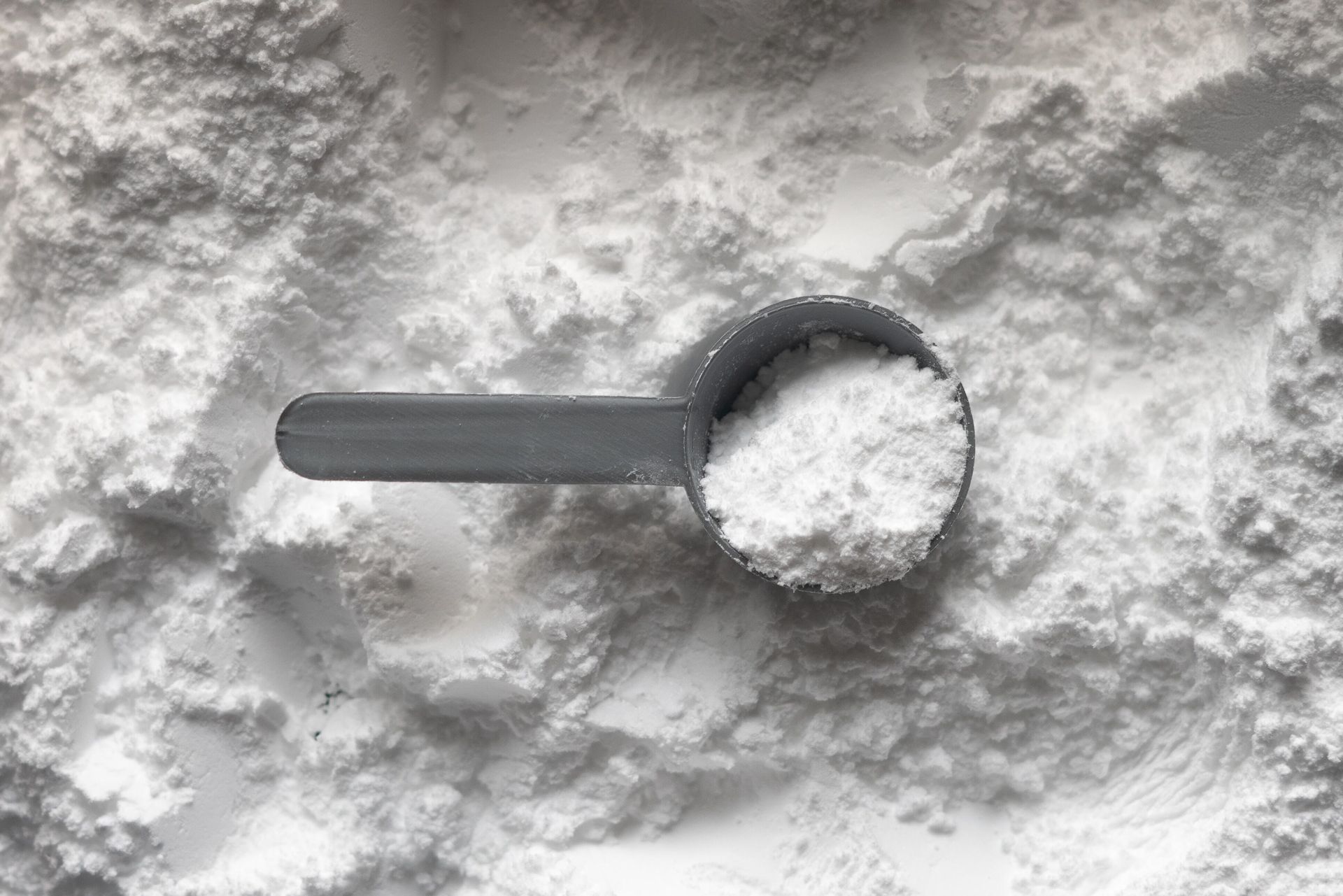 A spoon filled with white powder is sitting on top of a pile of white powder.