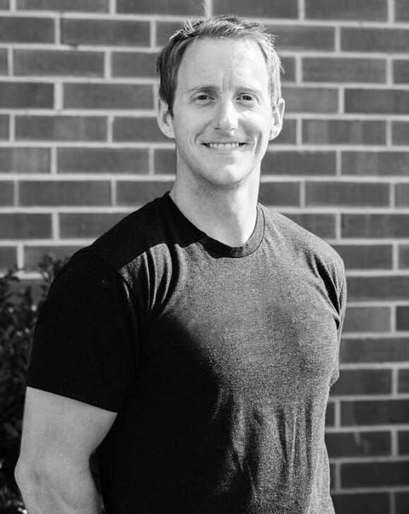 A man in a black shirt is standing in front of a brick wall.
