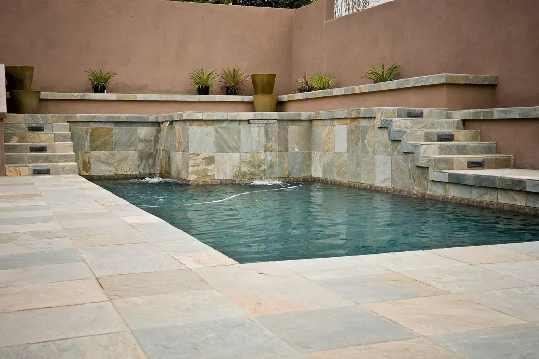 Pool with stone walls and steps, water flowing from tiered stonework. Earth tone walls.