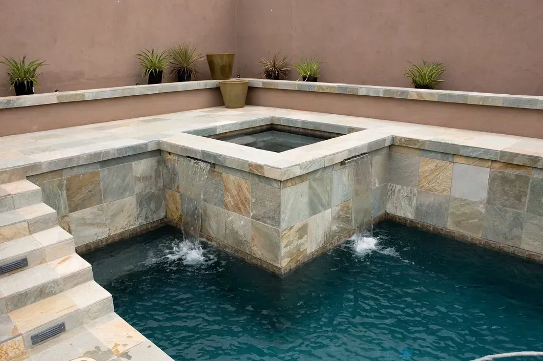 Stone-lined pool with built-in jacuzzi and waterfalls. Steps lead into the water.