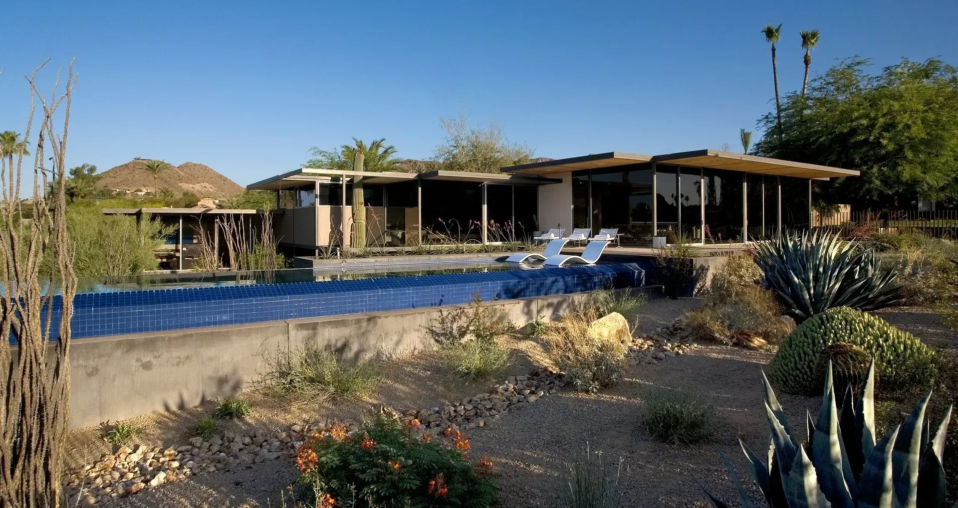 Modern house with a long pool, desert landscaping, and mountain backdrop.
