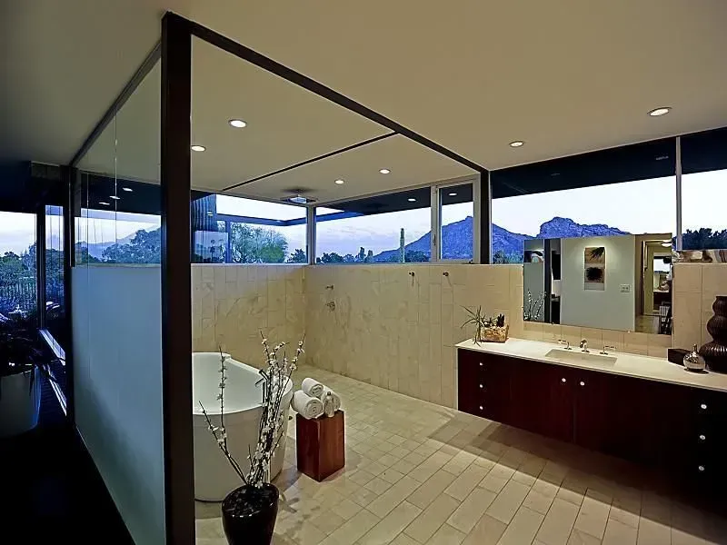 Modern bathroom with large windows, freestanding tub, vanity, and stone walls.